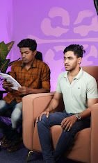 Two hosts recording a podcast against a purple-lit backdrop